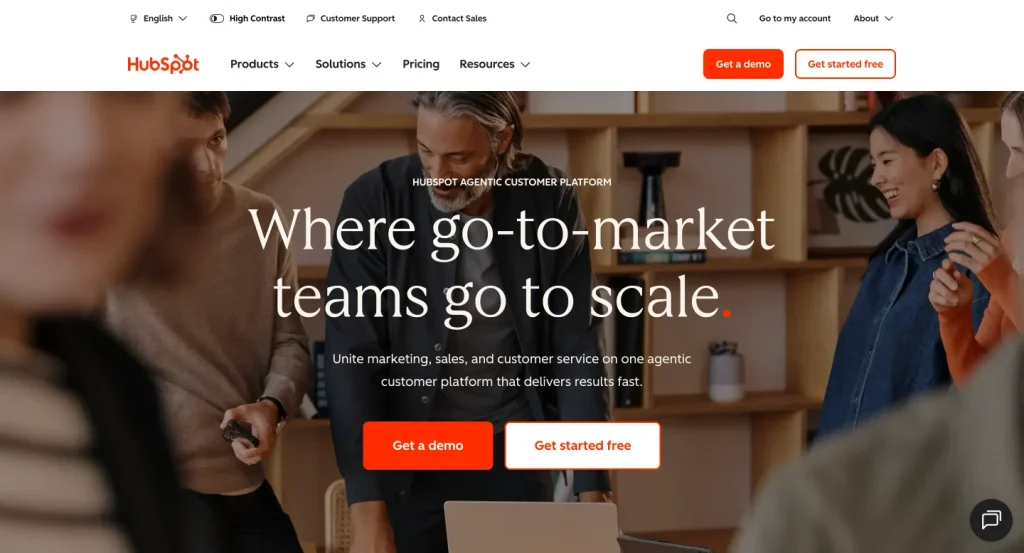 HubSpot’s homepage hero shows a clean SaaS layout with a bold navigation bar, warm team-focused background image, large headline, and clear CTA buttons for demo and free signup.